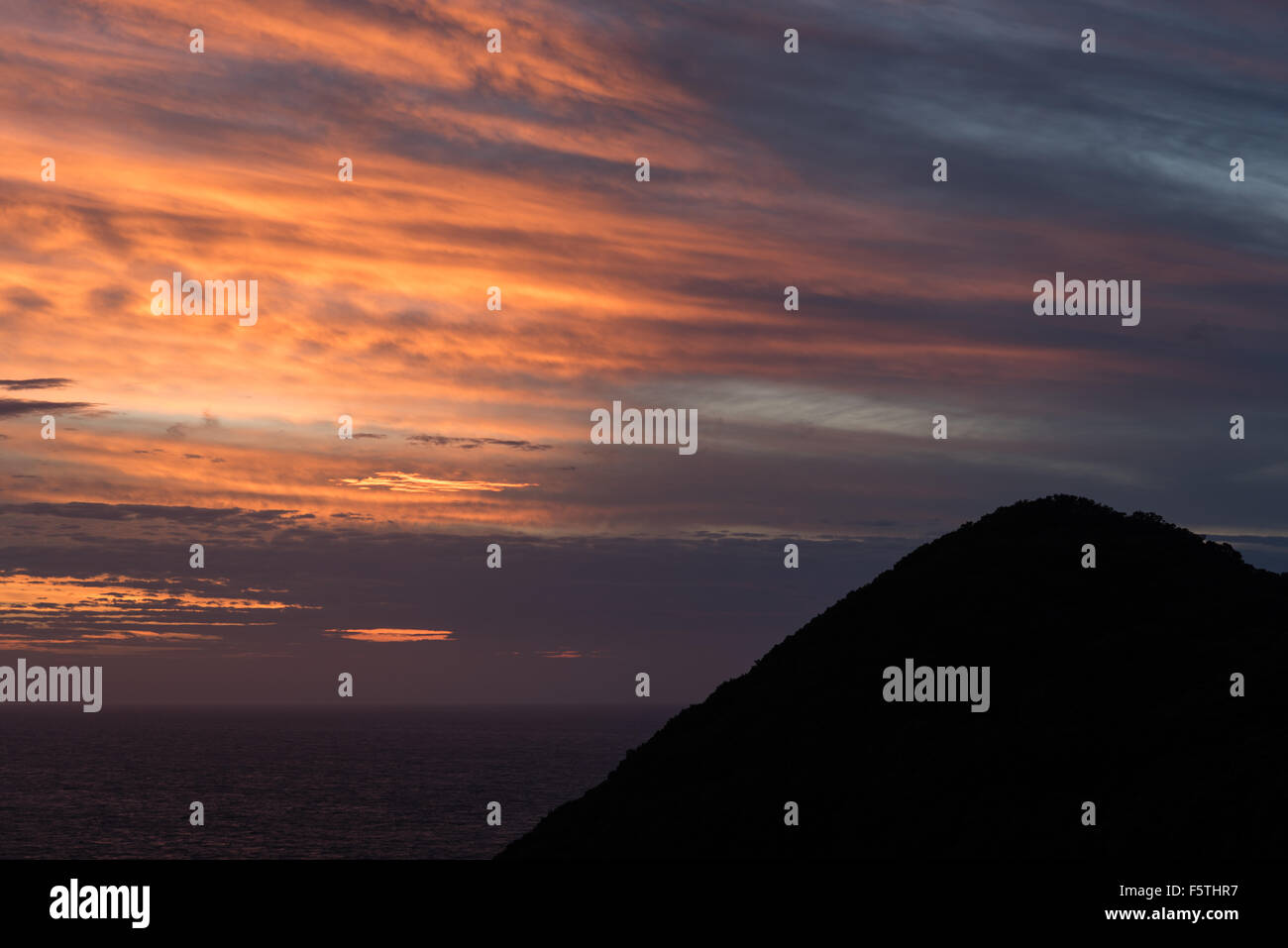 A beautiful colorful sunset over the ocean with a mountain in ...