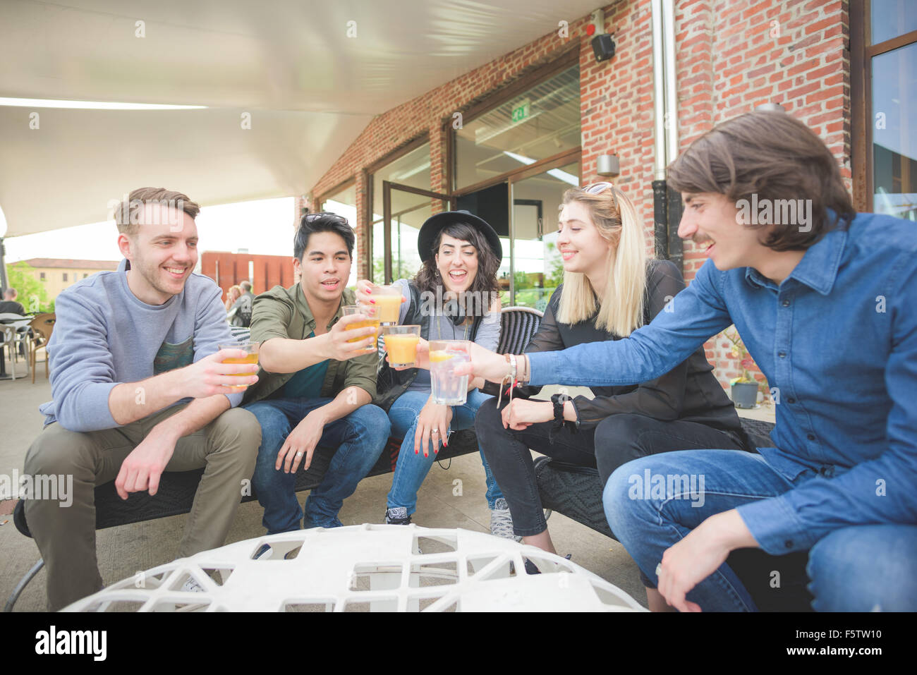 Group of young multiethnic friends sitting in a bar making a toast with beers, having fun - relaxing, happy hour, friendship concept Stock Photo
