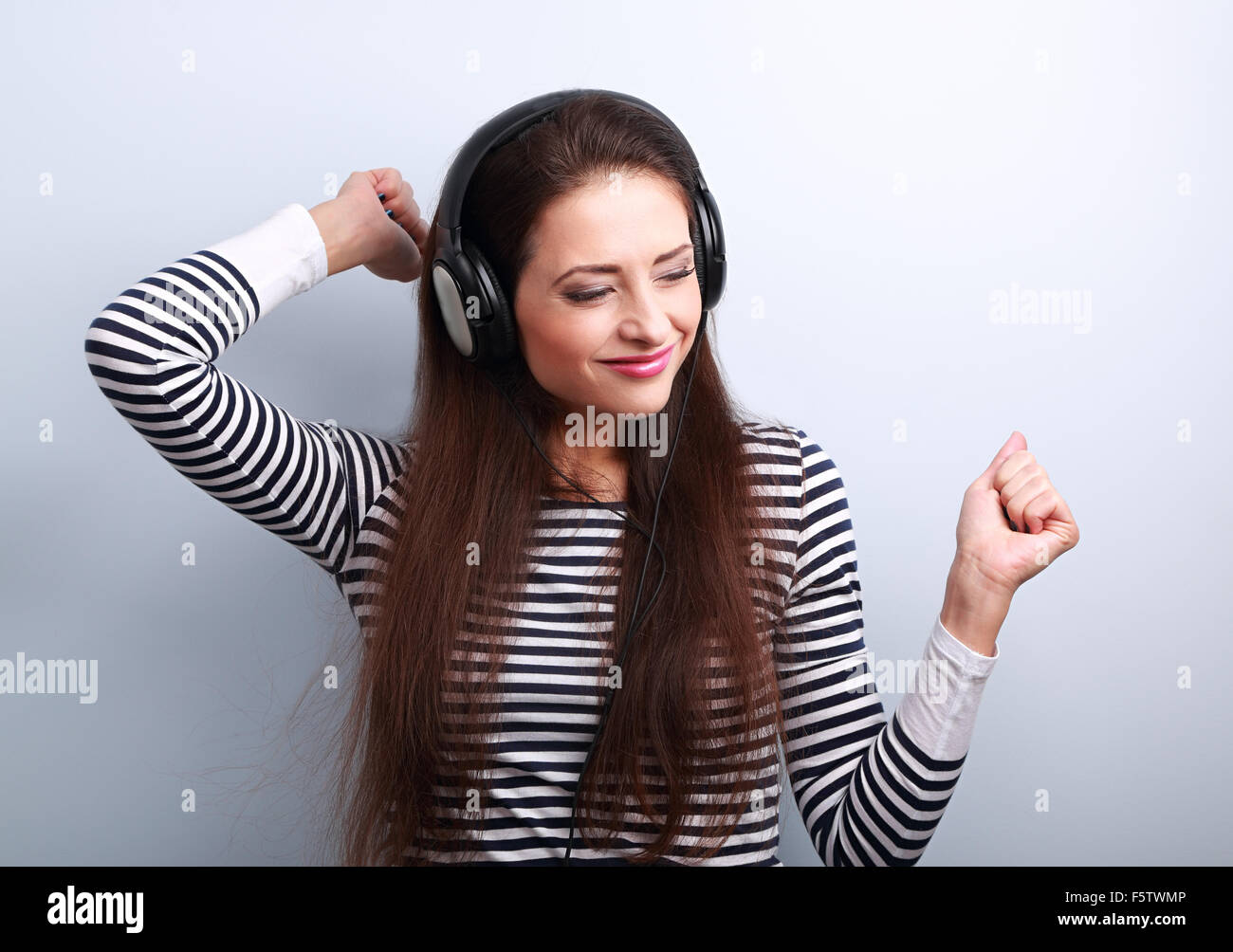 Young beautiful woman listening the music from headphones with dancing on blue background Stock Photo