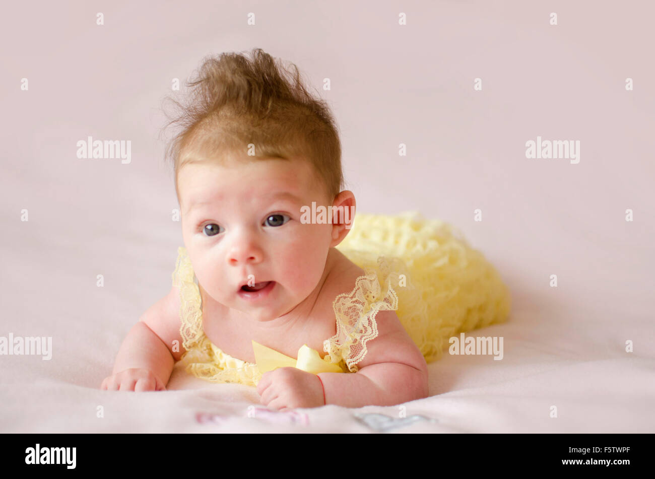 beautiful baby girl lying on tummy wearing yellow dress Stock Photo
