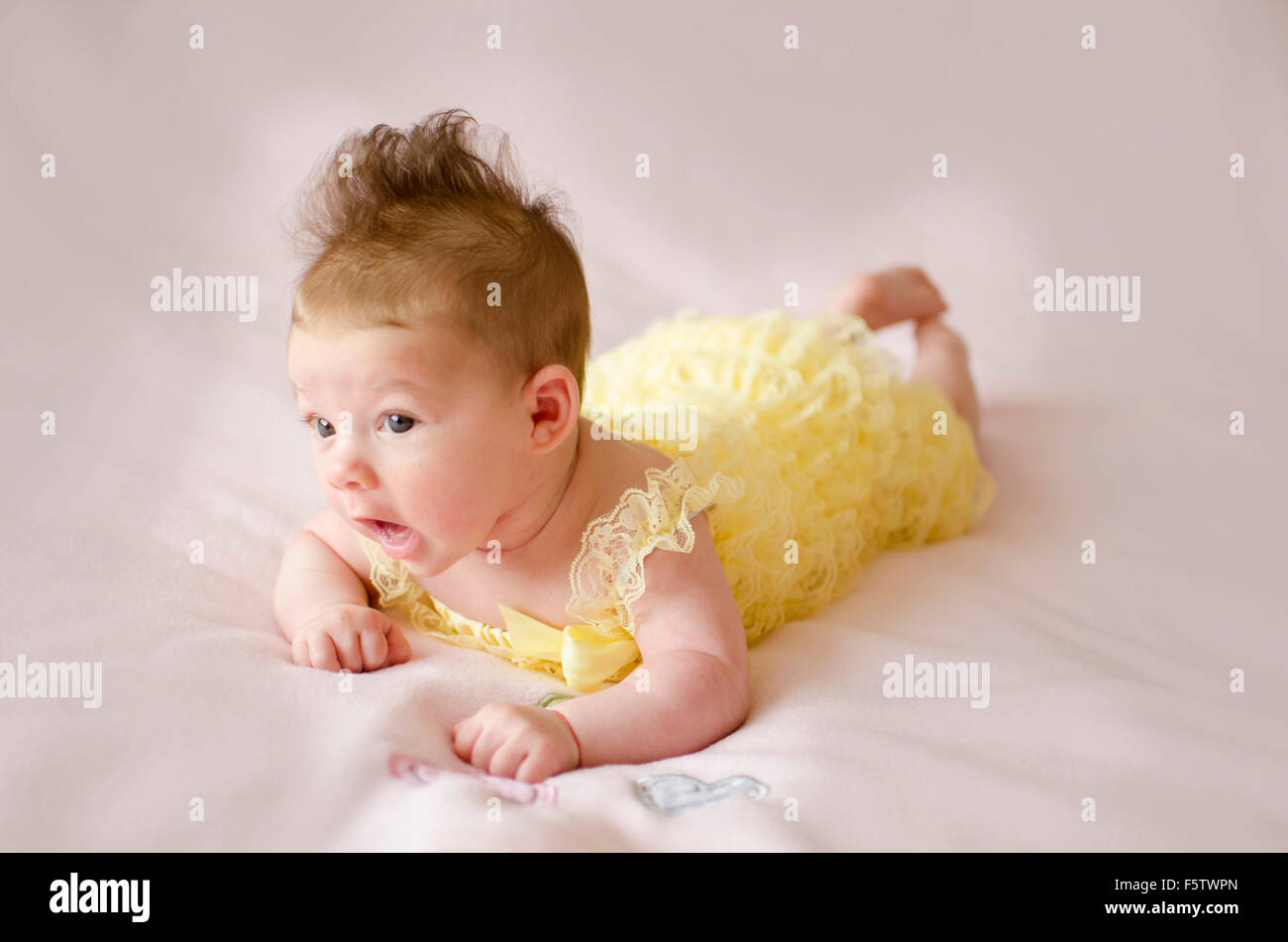 beautiful baby girl lying on tummy wearing yellow dress Stock Photo