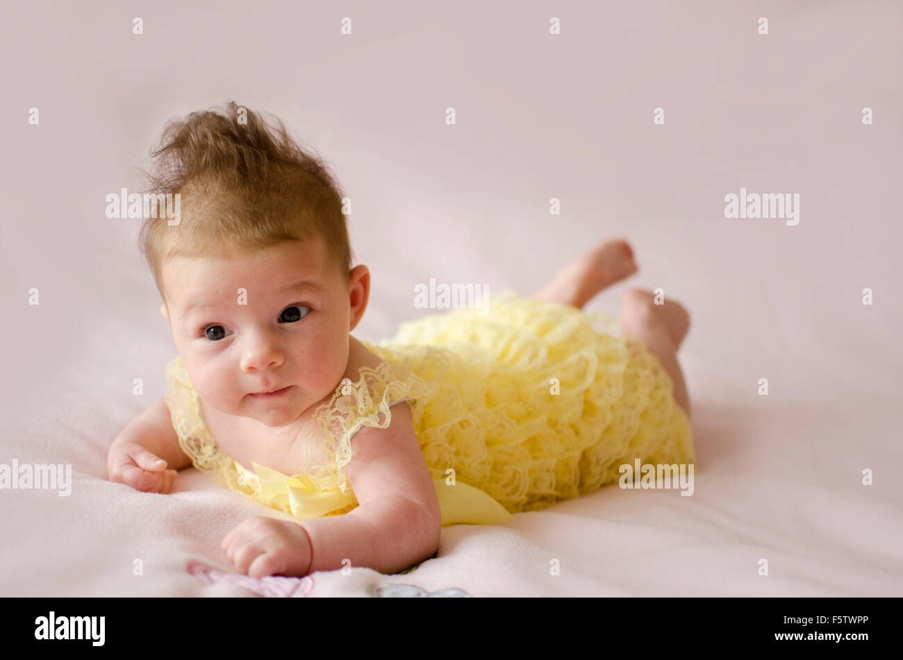 beautiful baby girl lying on tummy wearing yellow dress Stock Photo