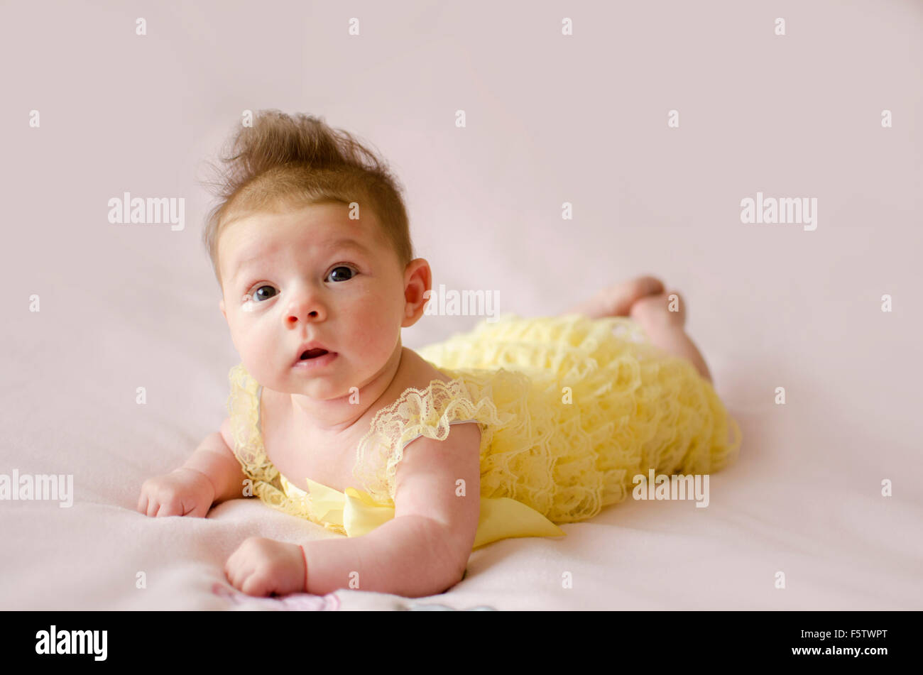 beautiful baby girl lying on tummy wearing yellow dress Stock Photo