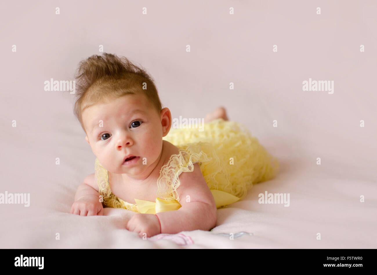 beautiful baby girl lying on tummy wearing yellow dress Stock Photo