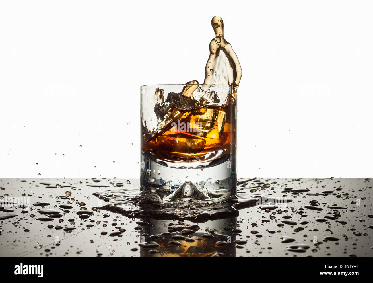 Glass filled with liquor and ice spilling over onto a black mirror like