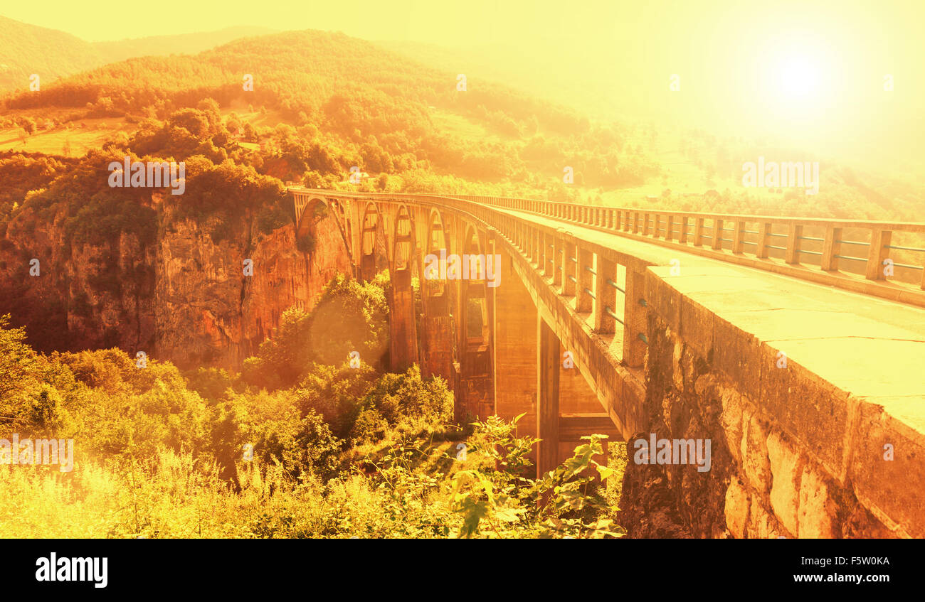 Old big bridge and view of river and green landscape in yellow light Stock Photo