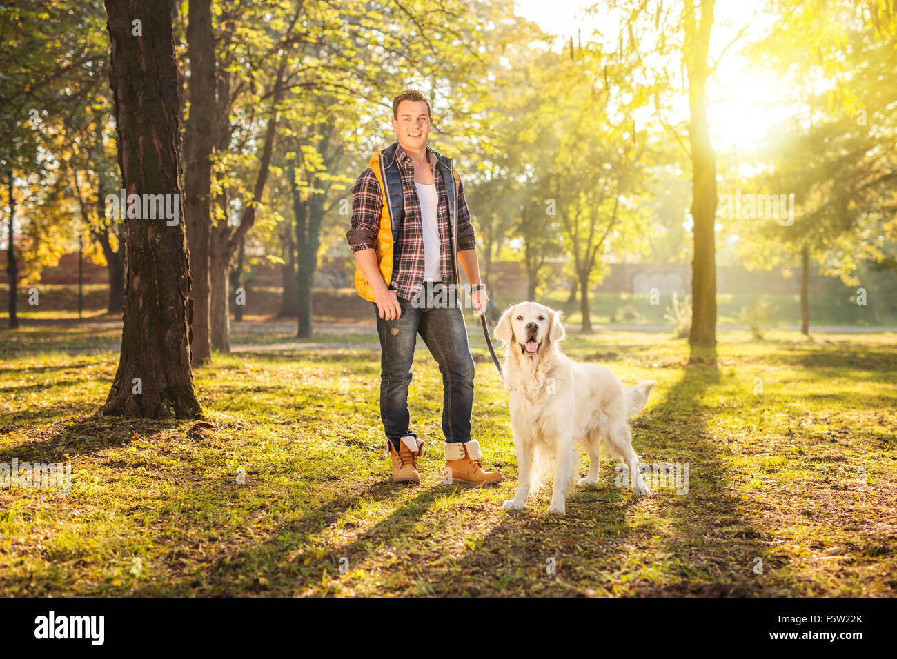 Young man standing in a meadow and posing with his dog on a sunny ...