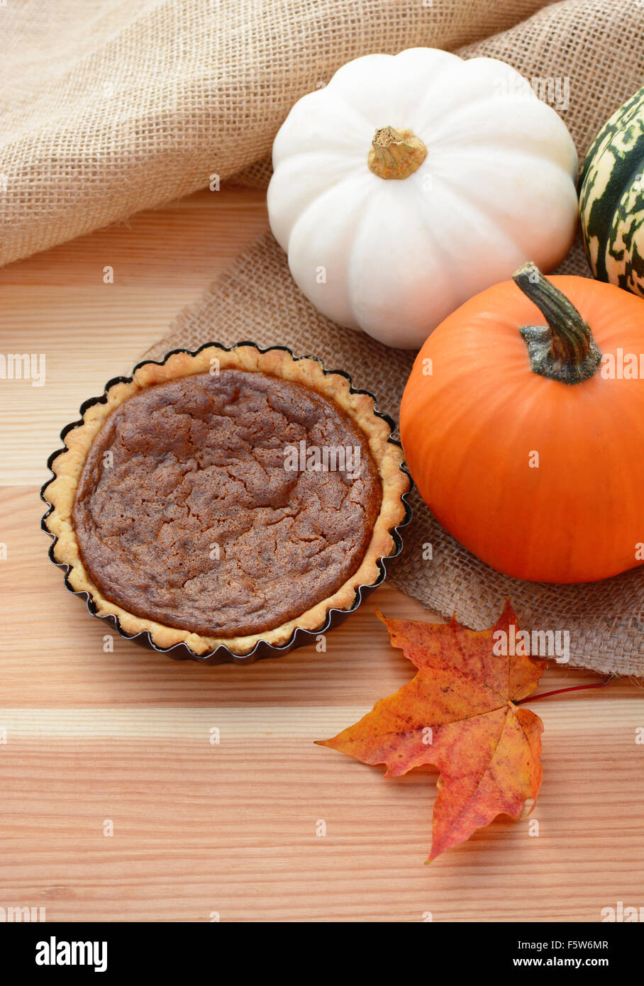 Mini pumpkin pie on a table with autumn gourds and red maple leaf Stock Photo