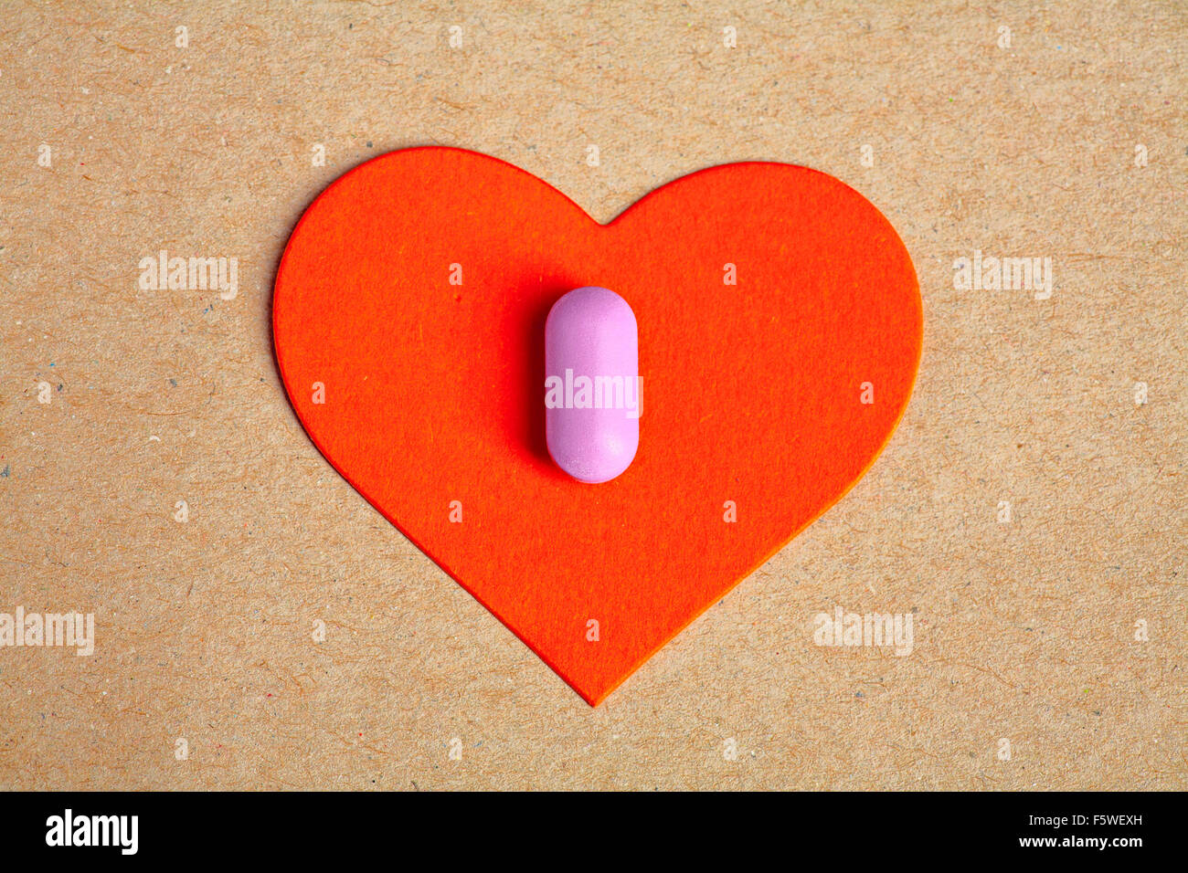 Red paper heart shape over craft paper with one small pink pill on