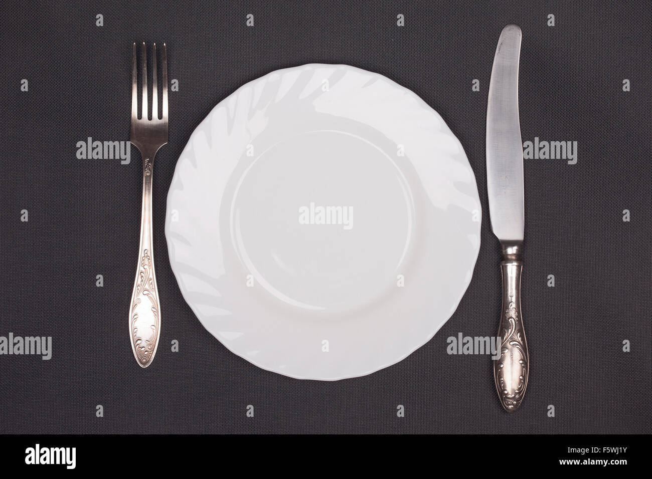 Plate, fork and knife top view on black cloth background Stock Photo