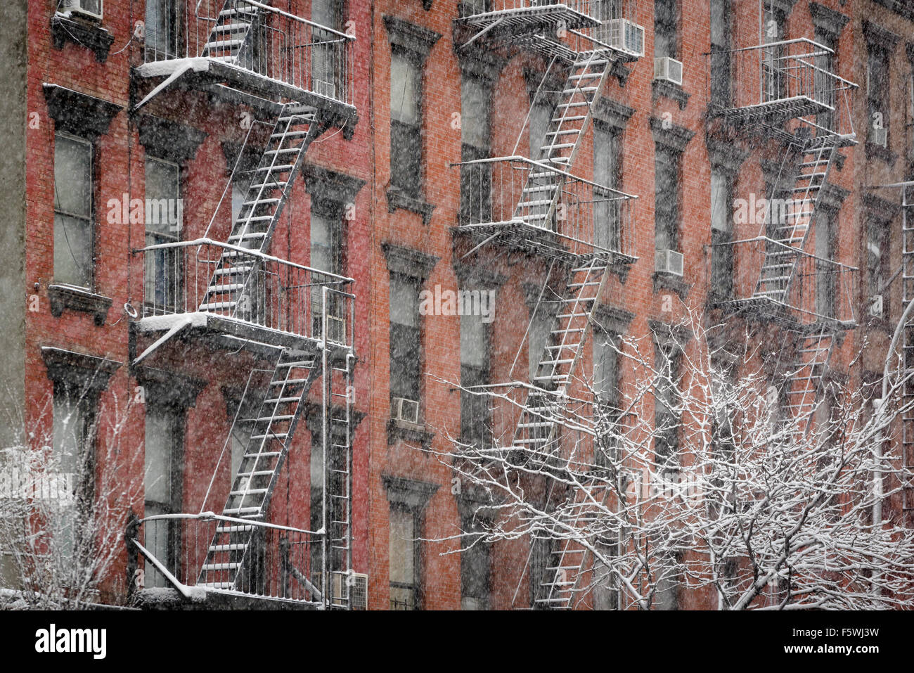 Facade of Chelsea brick building with fire escapes covered in snow during a winter snowfall, Manhattan, New York City Stock Photo
