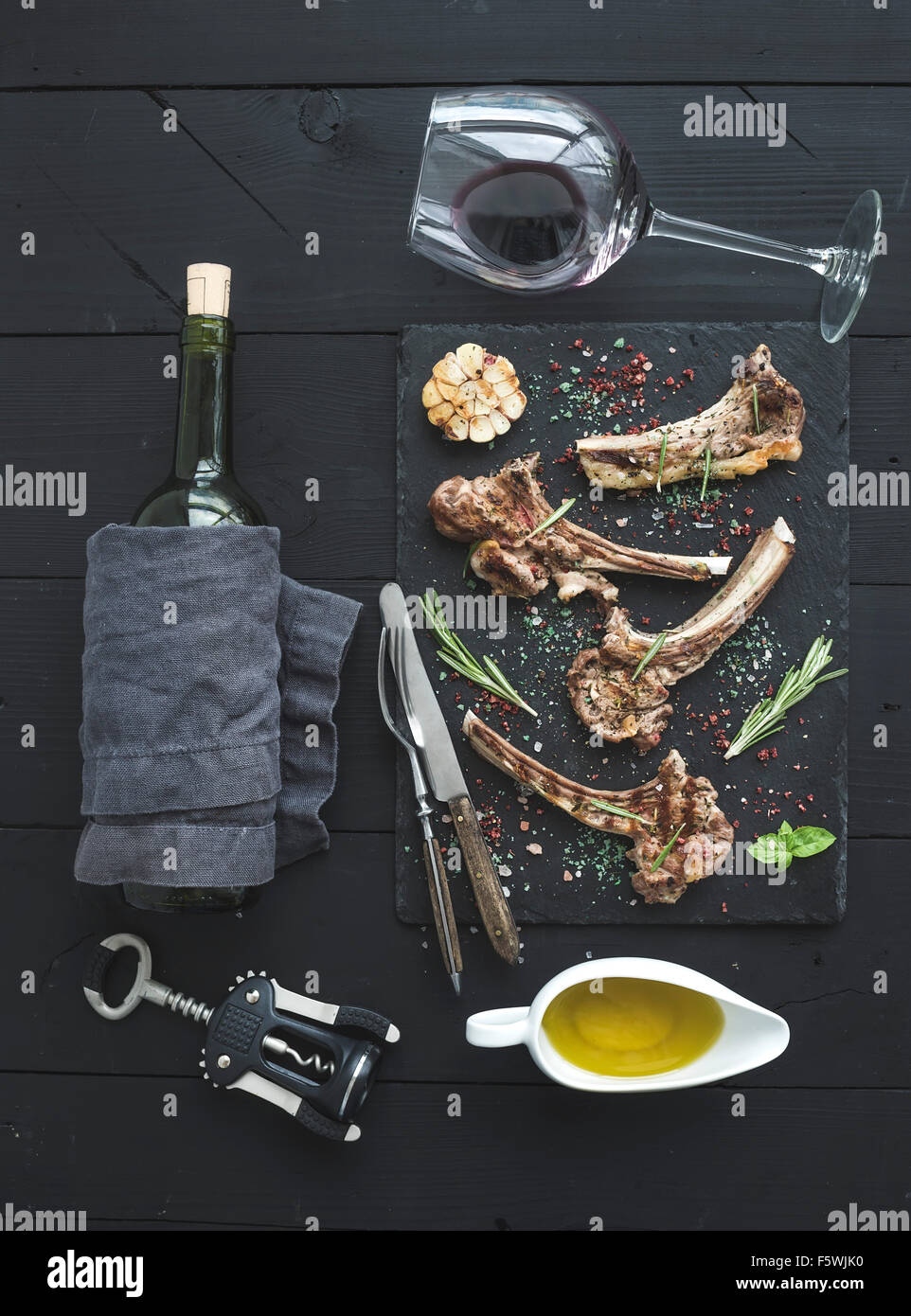 Grilled lamb chops. Rack of Lamb with garlic, rosemary and spices on slate tray, wine glass, oil
