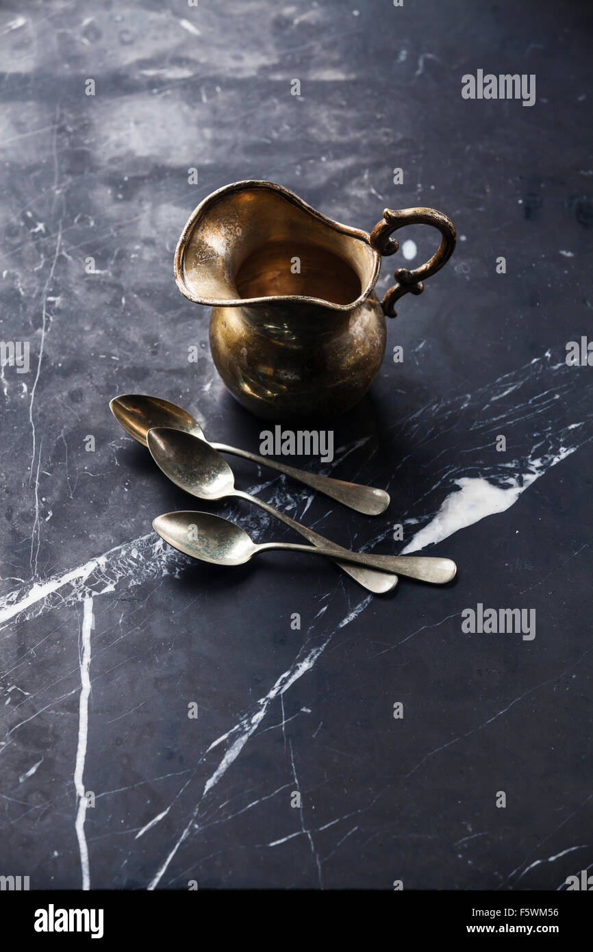 Vintage Kitchenware Silver milk jug and teaspoons on black marble background Stock Photo