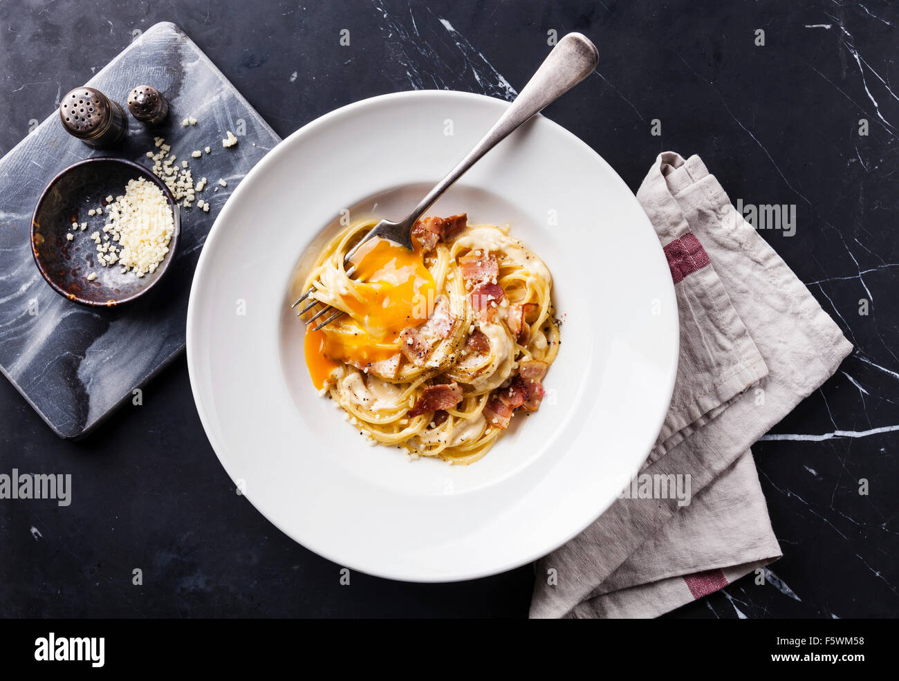Pasta Carbonara on white plate with parmesan and yolk on black marble background Stock Photo