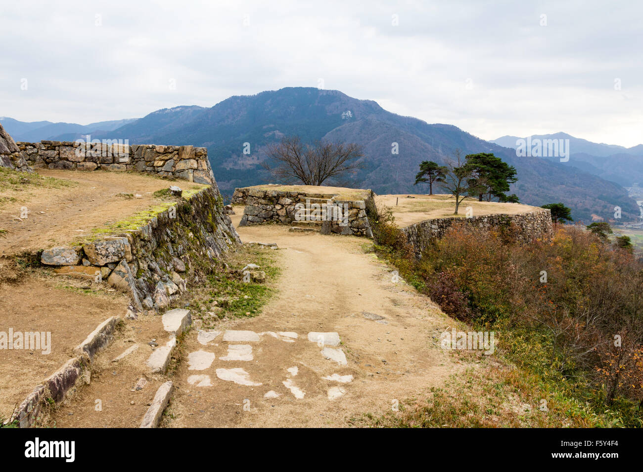 Japan, Takeda mountain top castle. Stone foundations for walls and buildings of the minami Senjo, with mountains beyond. Grey sky, overcast. Stock Photo