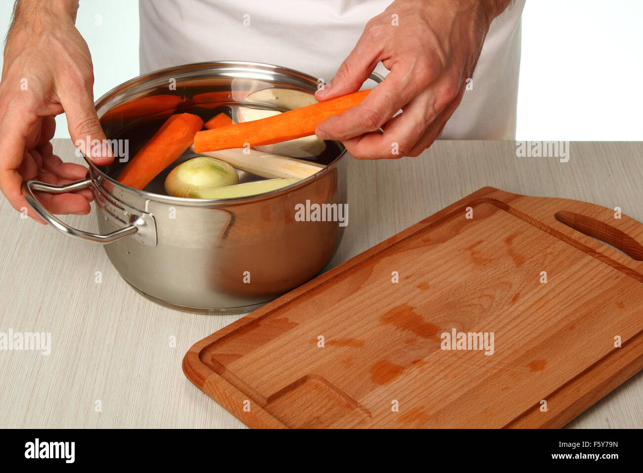 Adding vegetables into saucepan. Making vegetables bouillon. Stock Photo