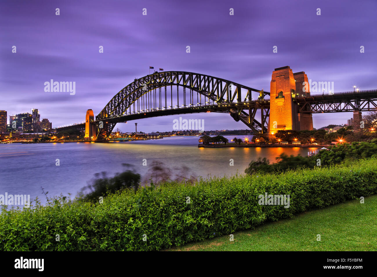 side view of famous Sydney Harbour bridge at sunset with illumination from green recreational park at milsons point with bushes Stock Photo
