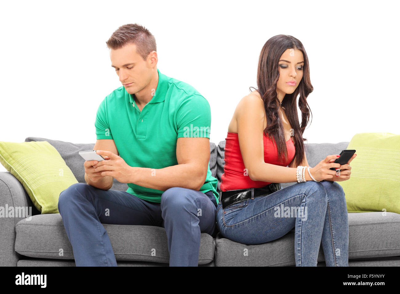 Young couple looking at their cell phones and ignoring each other seated on a gray sofa isolated on white background Stock Photo