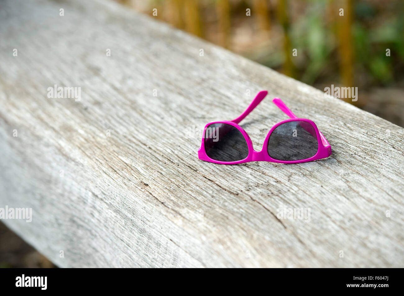 Childs pink sunglasses on a wooden seat in an english garden Stock Photo