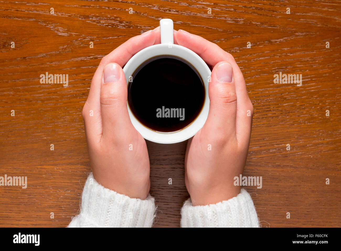 Women's arms wrapped around a hot cup of coffee on the table Stock Photo