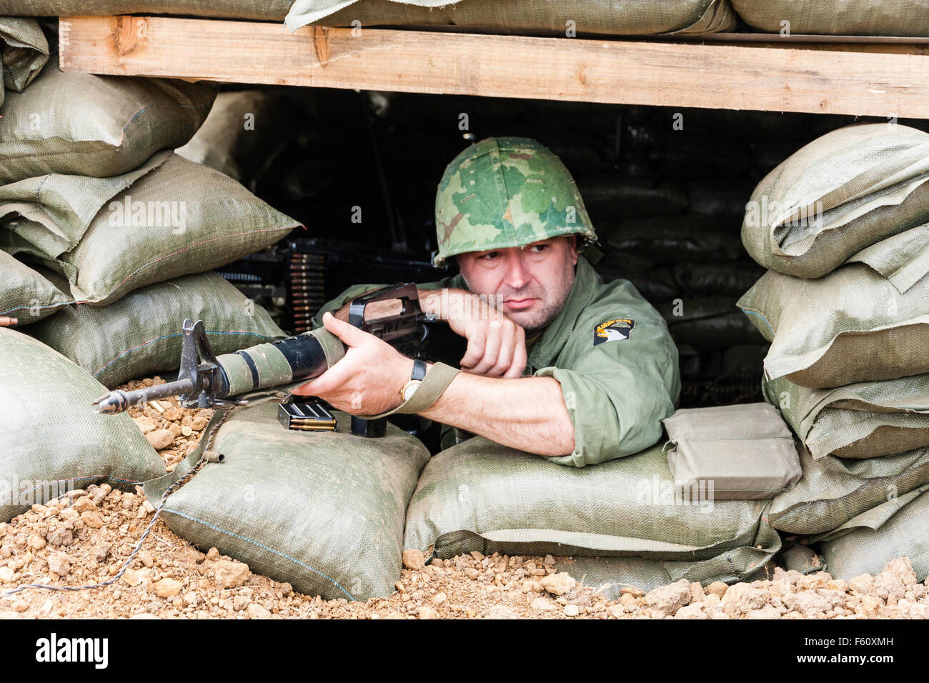 Vietnam war 'rolling thunder' re-enactment. US Marine in bunker, leaning on M16 rifle, with bored expression while on guard duty. Facing. Stock Photo
