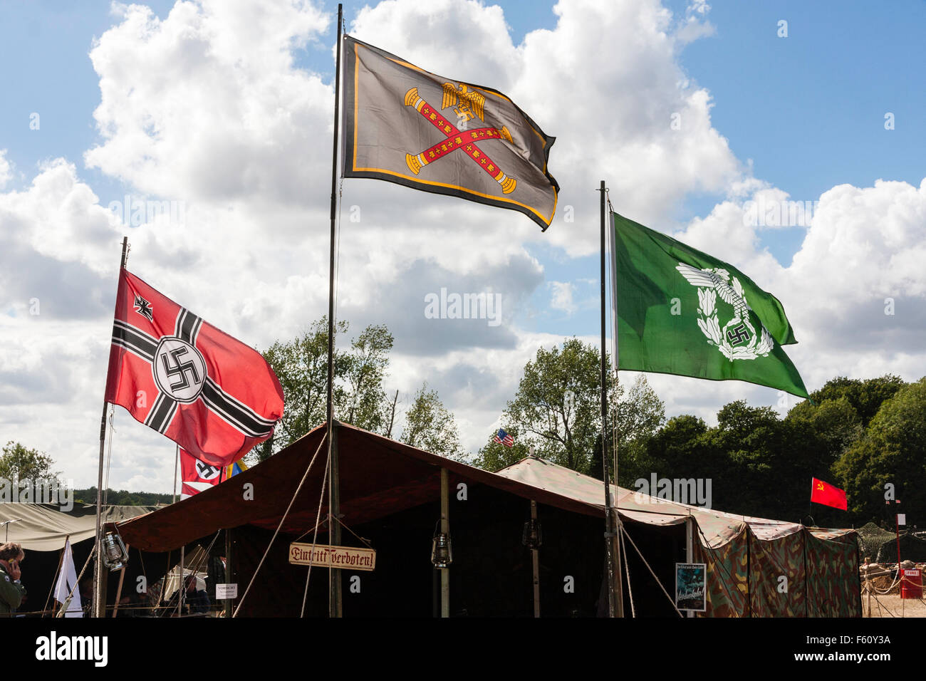 World War Two re-enactment. Third Reich Reihskriegsflagge, battle flag and two German army flags flying above tent. Backlit. Stock Photo