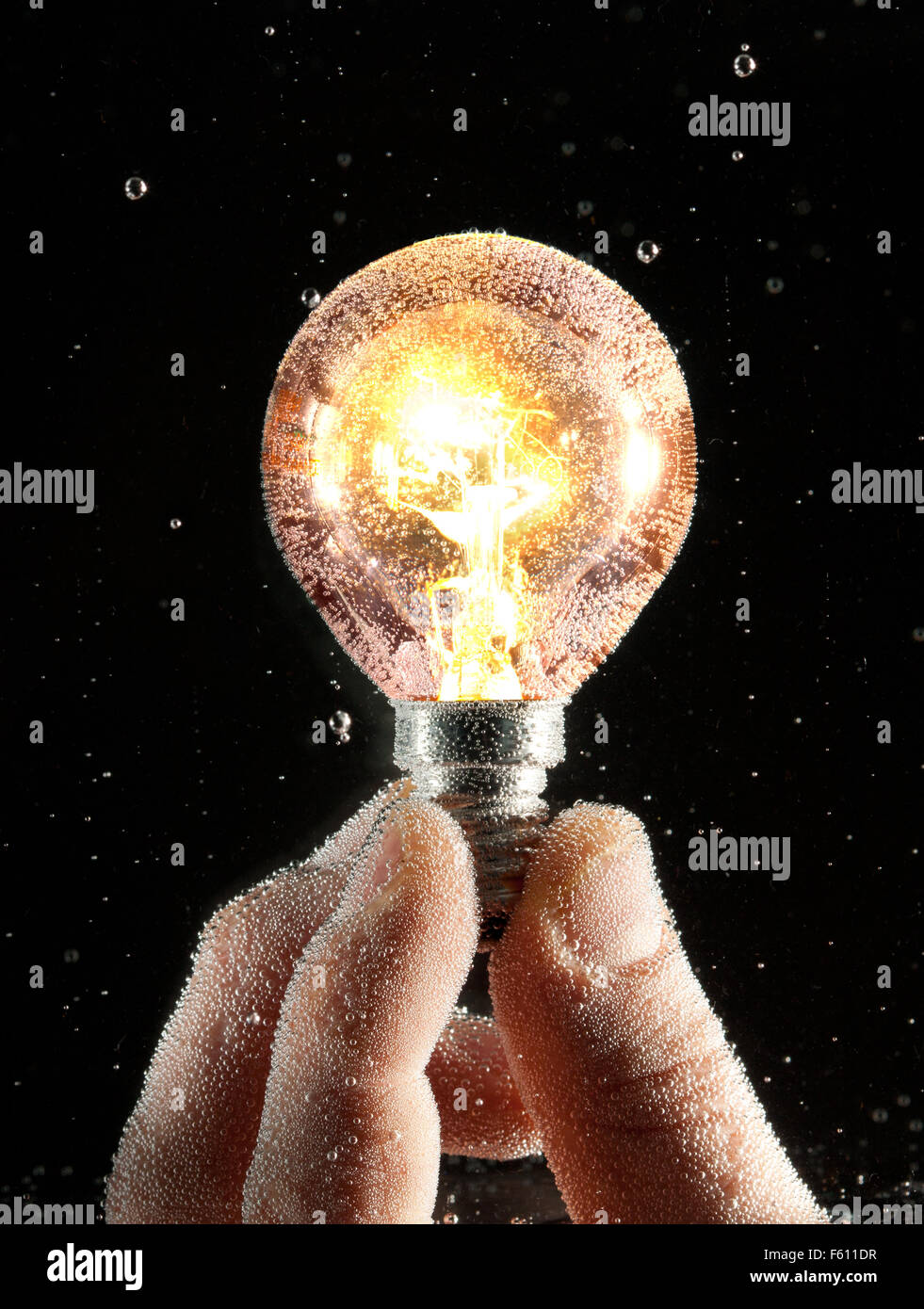 Hand holding turned-on conventional bulb under water Stock Photo