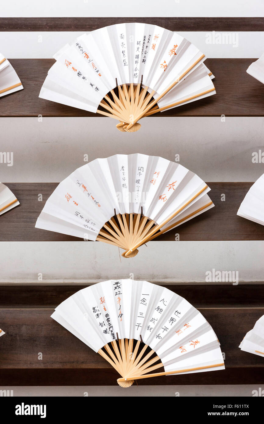 Japanese open religious fans, sensu, arranged on rack display stand. Pale natural wood colour, with white leaves containing Japanese kanji characters. Stock Photo
