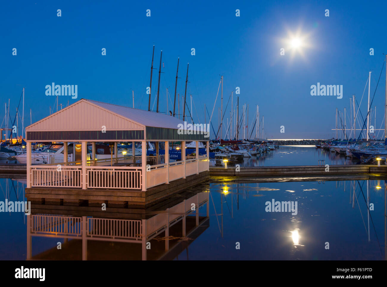 A covered dock and yachts at the Bronte Outer Harbour Marina at dusk during a full moon. Bronte, Oakville, Ontario, Canada. Stock Photo