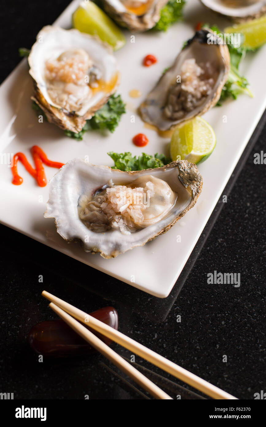 Angled view of oysters on the half-shell on a rectangular plate with chopsticks. Stock Photo