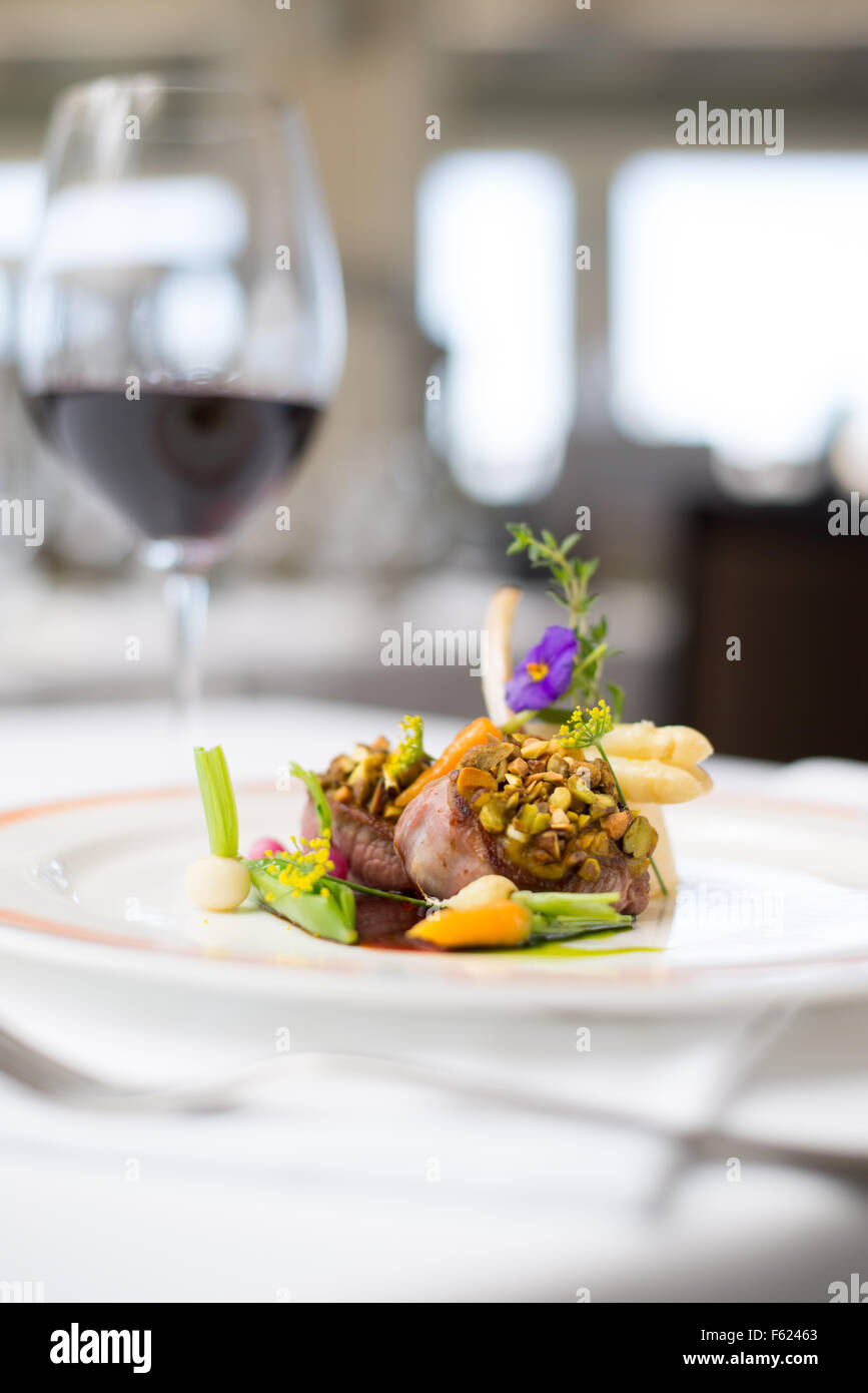 Eye-level view of pistachio-crusted lamp chops with vegetable garnish in a restaurant environment. Stock Photo
