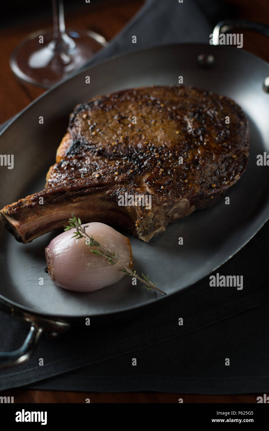 Angled-view of steak on a metallic dish with onion and thyme garnish in a restaurant setting. Stock Photo