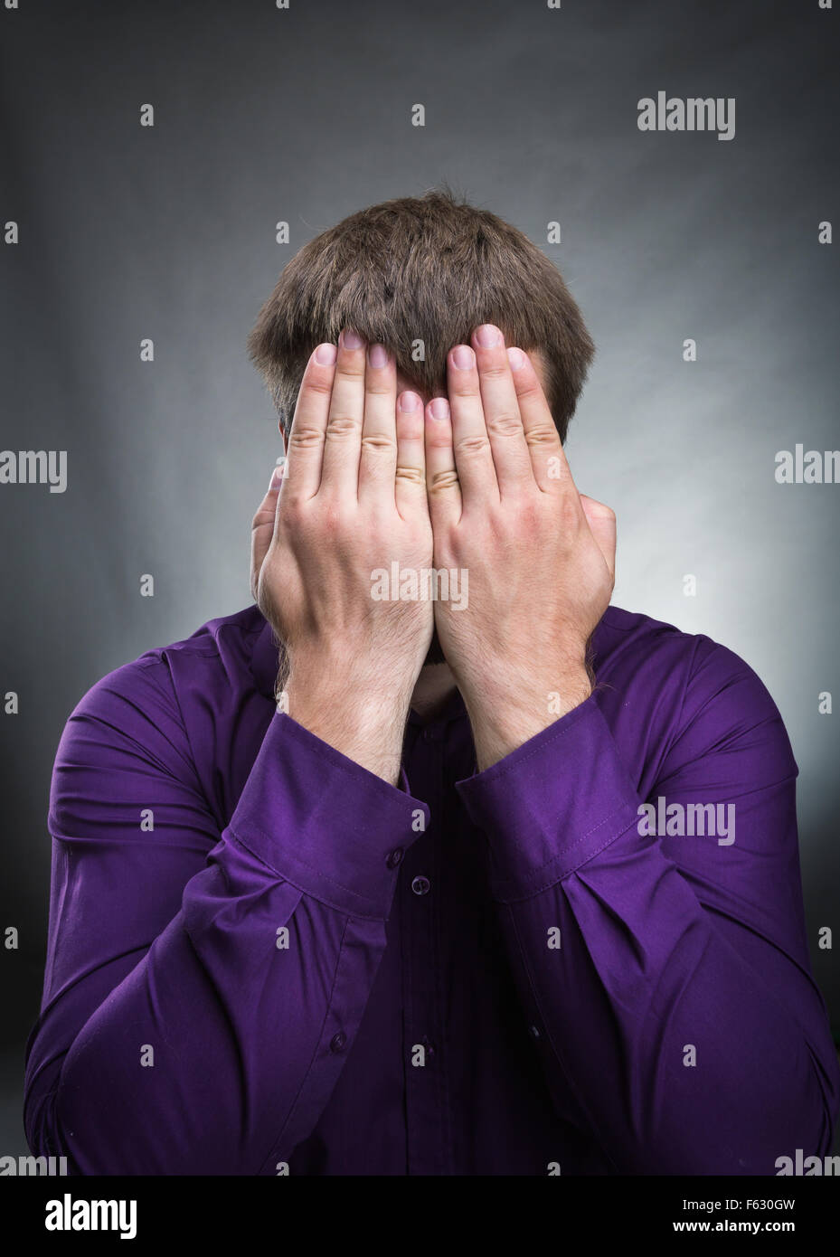 Man covers his face with hands over grey background Stock Photo Alamy