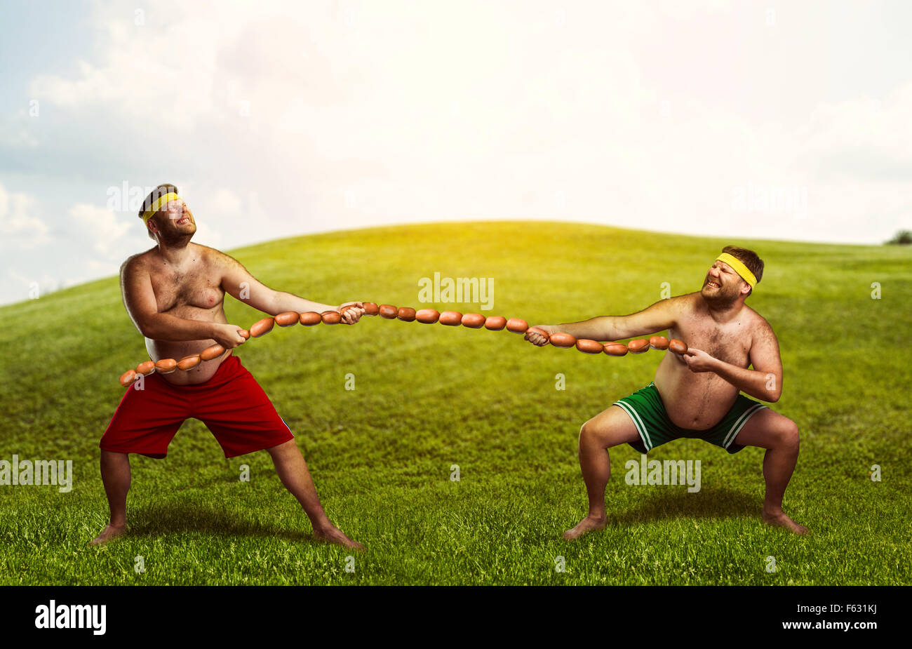 Two men fighting for sausages in the meadow Stock Photo