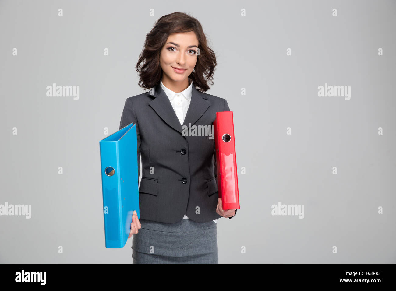 Beautiful young curly happy woman in gray suit holding red and blue binders Stock Photo