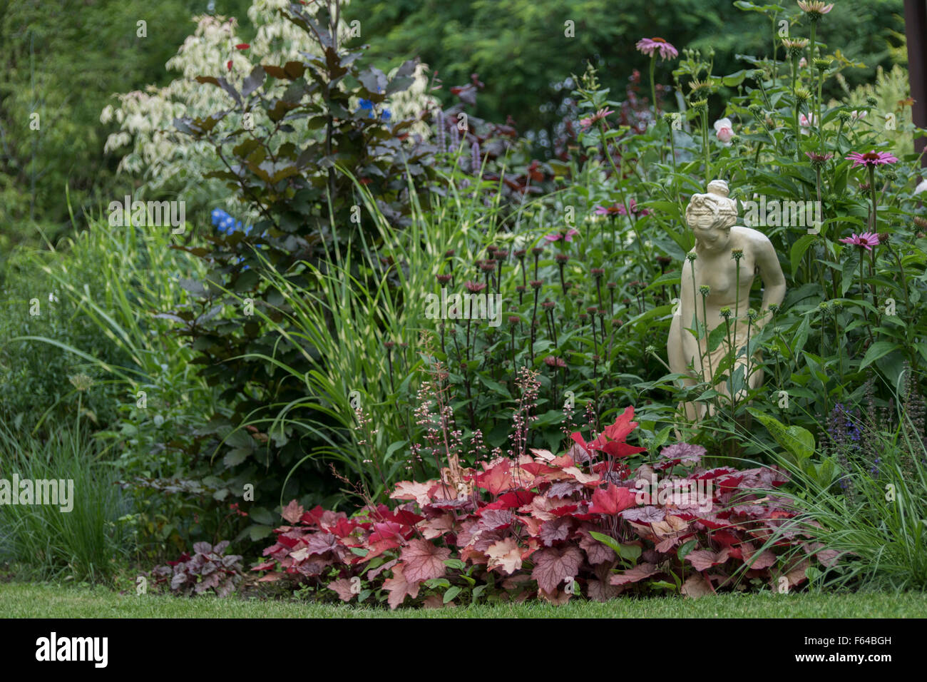 Summer perennials surrounding a stone statue. Stock Photo