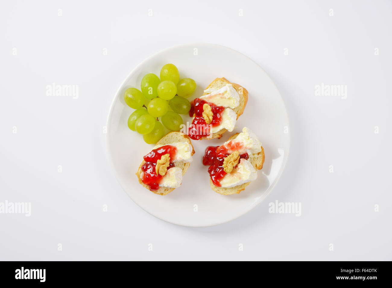 slices of fresh bread with brie cheese, walnuts, jam and grapes on white plate Stock Photo