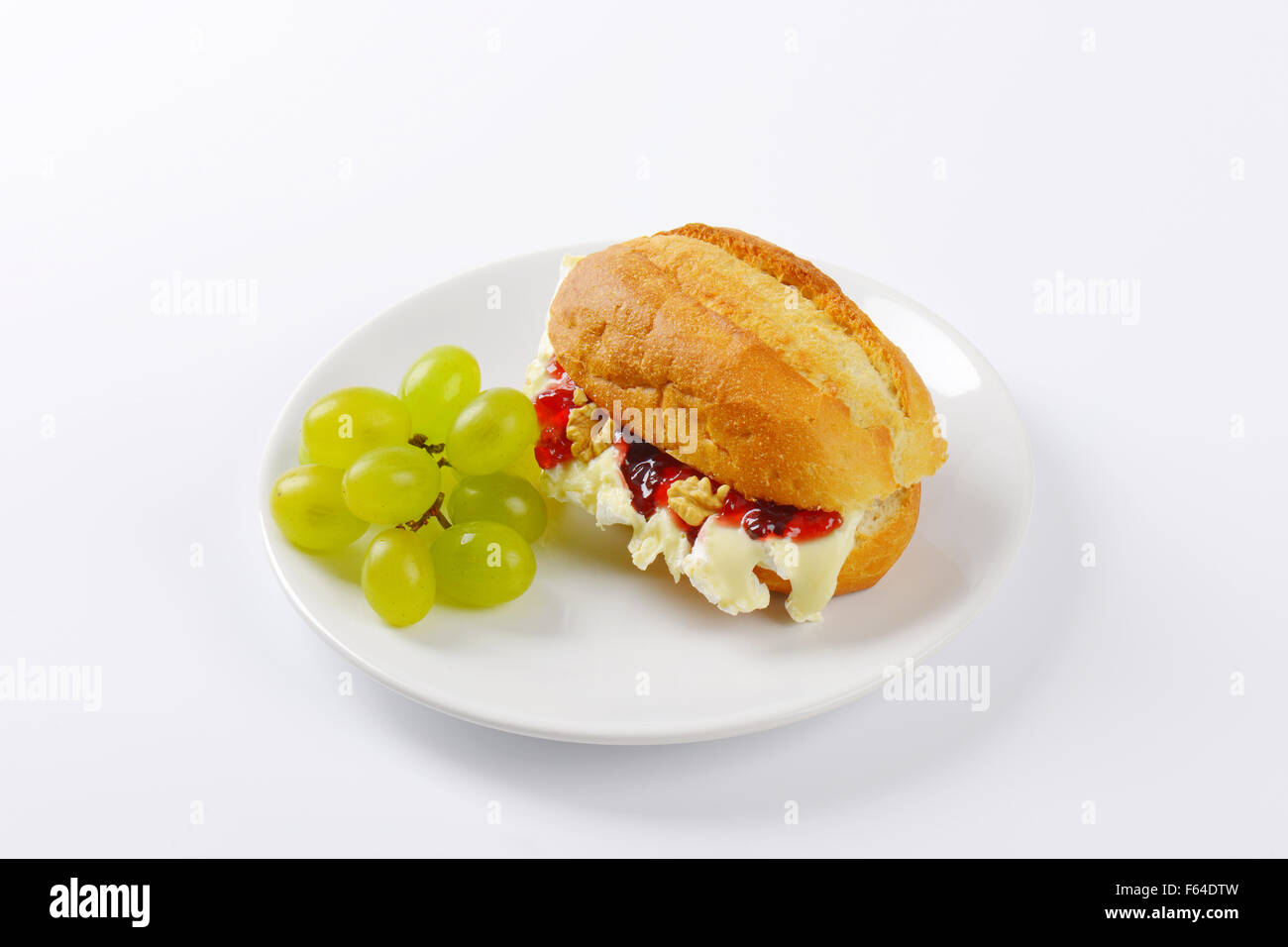 small baguette with brie cheese, walnuts, jam and grapes on white plate Stock Photo