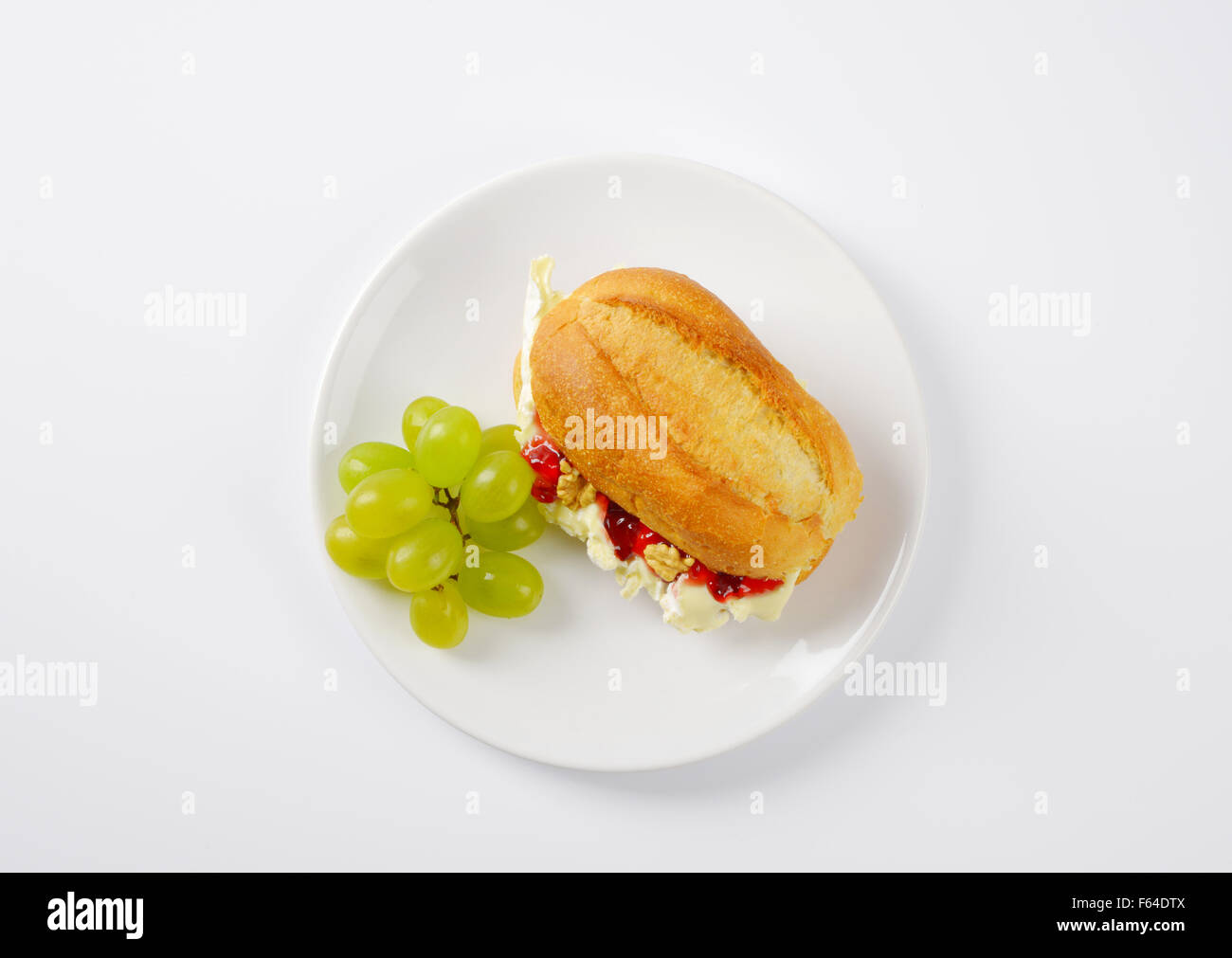 small baguette with brie cheese, walnuts, jam and grapes on white plate Stock Photo