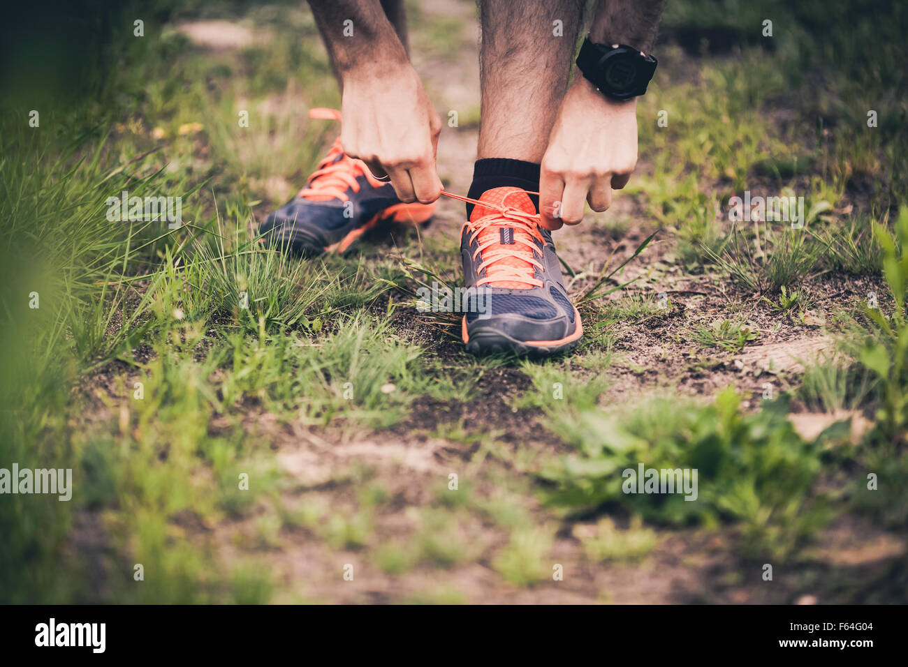 Runner tying sports shoe. Man running on cross country path in summer nature. Young athlete male training and fitness workout Stock Photo