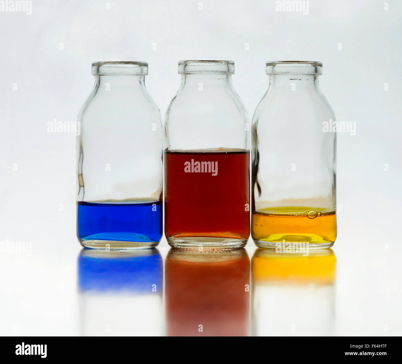 3 bottles with blue red and yellow liquid back lit luminous quality soft faded reflection muted soft grey background Stock Photo