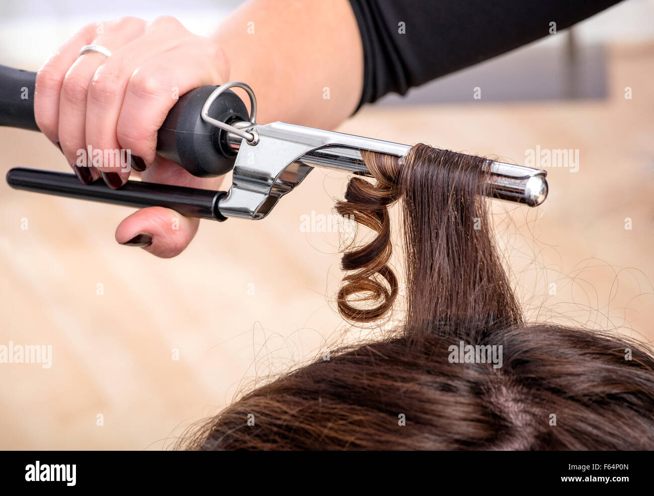 Hairstylist using a curling iron or tongs to firm ringlets in the long brown hair of a female client Stock Photo