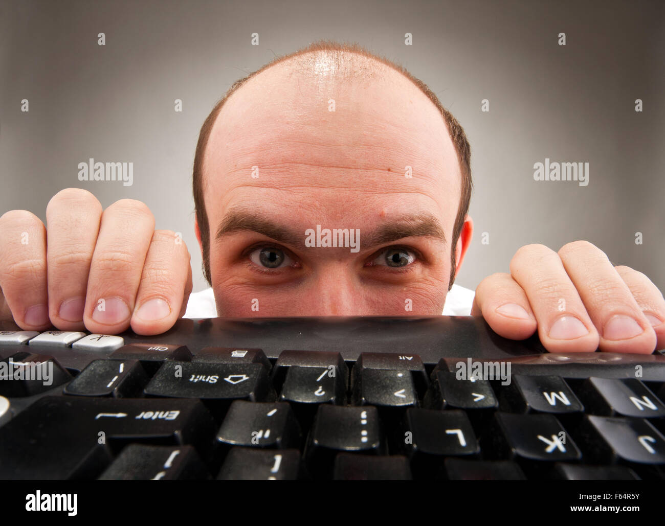Timid nerd hiding under computer keyboard. Wide angle Stock Photo Alamy