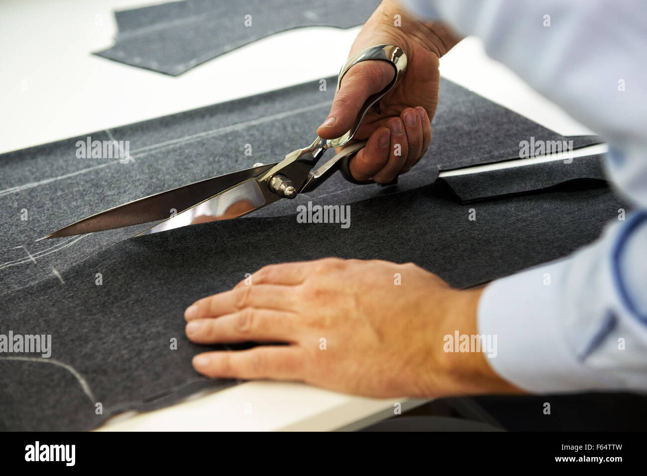 Tailor cutting out the marked pattern on dark fabric with large scissors on the workbench in his shop, close up view of his hand Stock Photo