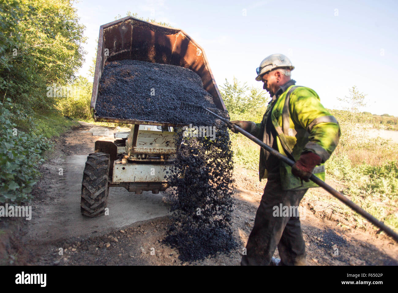 a workman empties hot asphalt onto a road from the back of a small dump truck Stock Photo