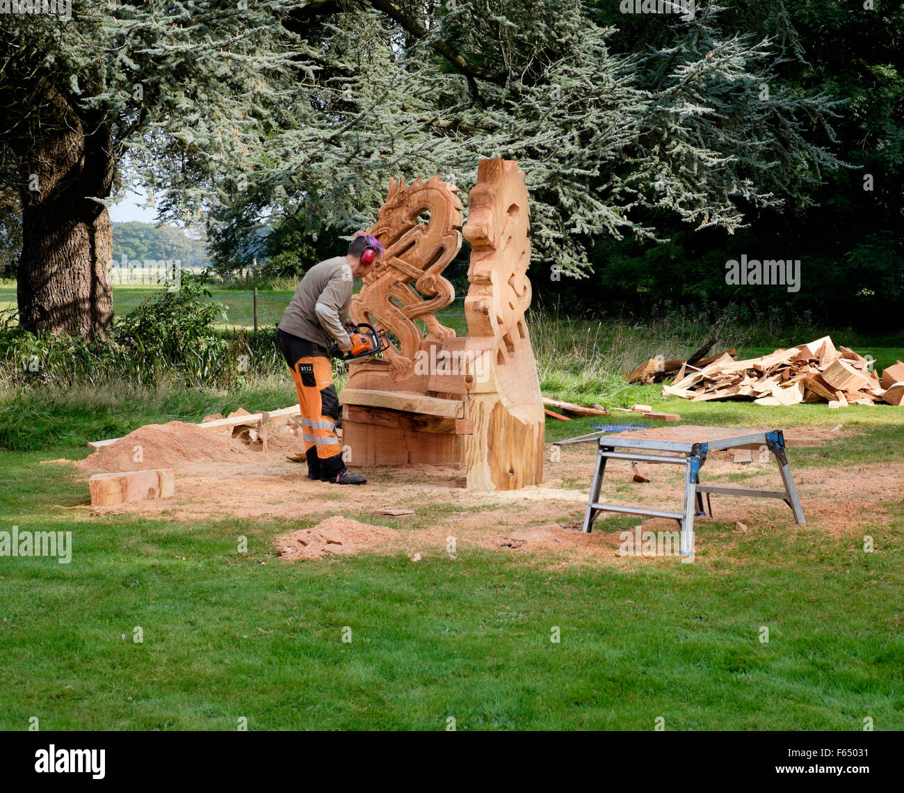 A chainsaw sculptor creating a dragon themed garden chair sculpture from a tree trunk at the Cranborne Chase Woodfair, Wiltshire Stock Photo