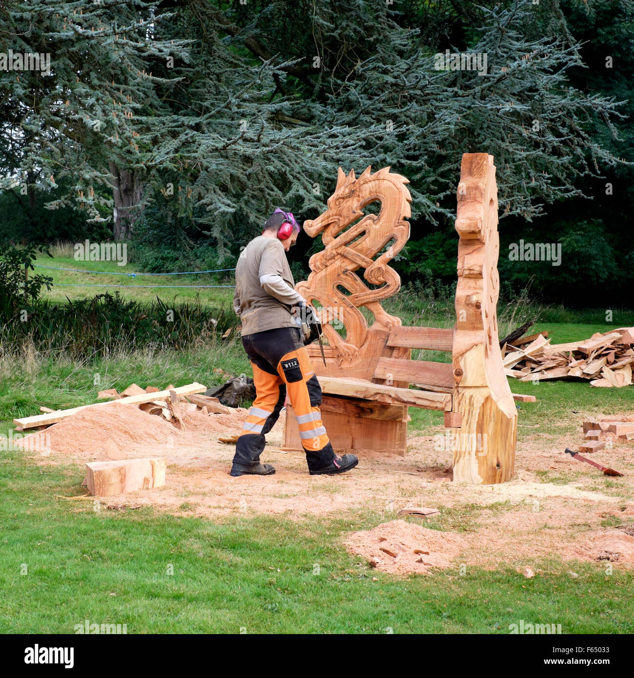 A chainsaw sculptor creating a dragon themed garden chair sculpture from a tree trunk at the Cranborne Chase Woodfair, Wiltshire Stock Photo