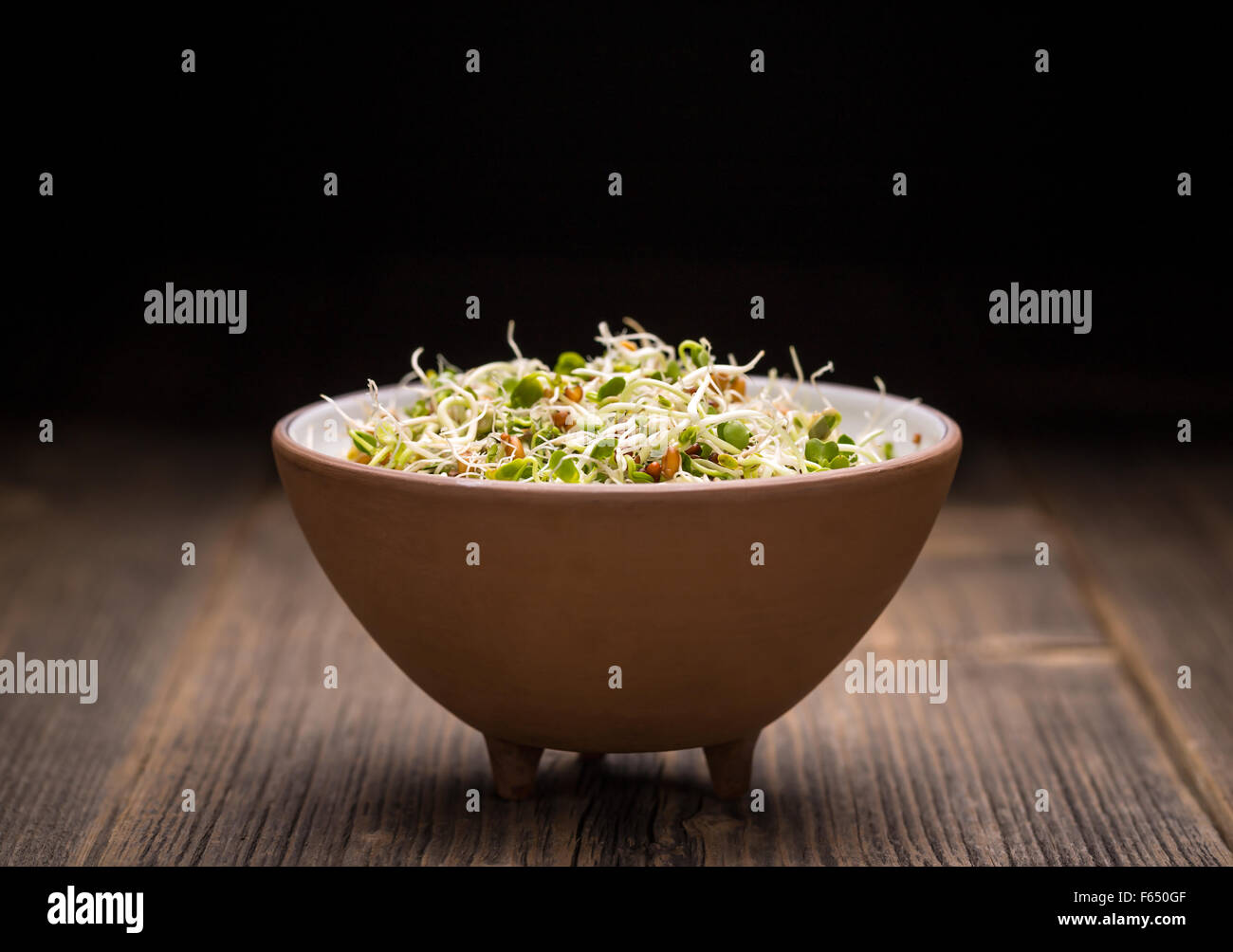 Mix of green young sprouts in bowl on wooden background Stock Photo