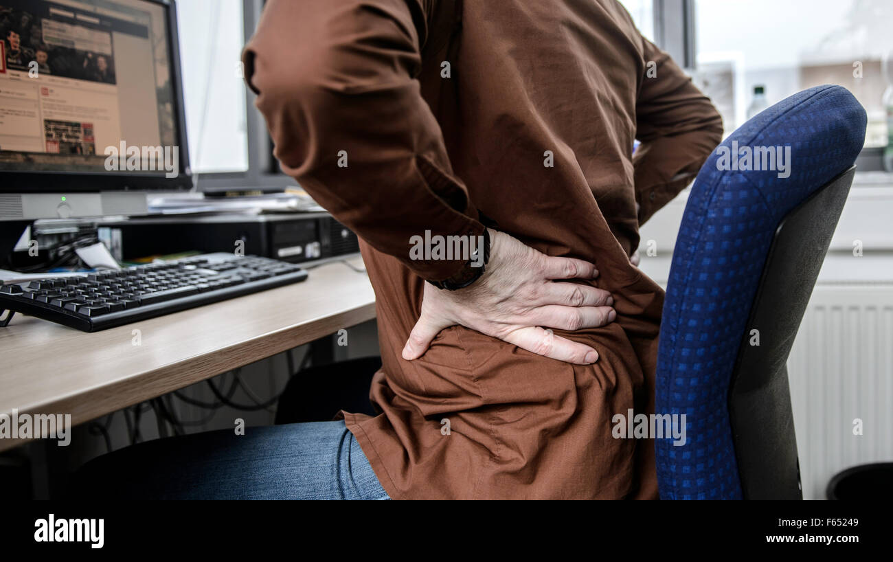 ILLUSTRATION An employee sits at his office desk and holds his hurting