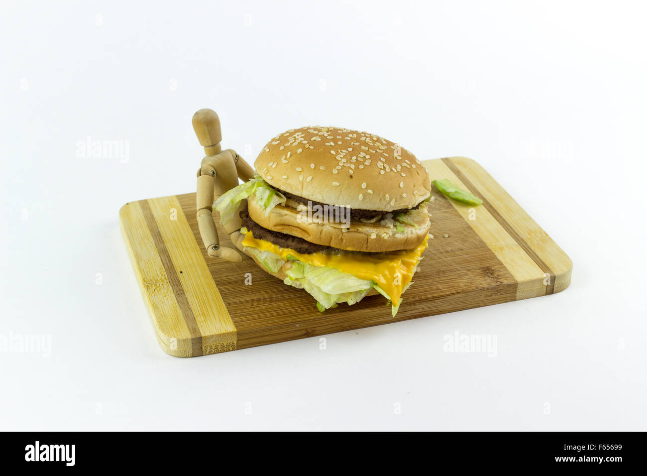 Wooden doll standing on a chopping board against a white background, holding a hamburger Stock Photo